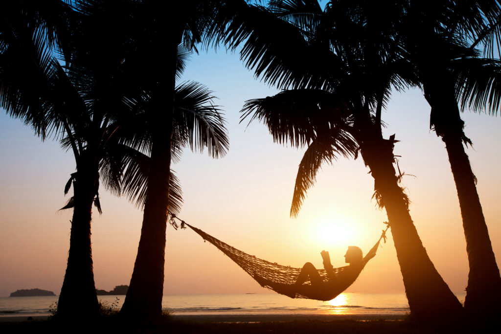 mujer en una hamaca en la playa lee un libro